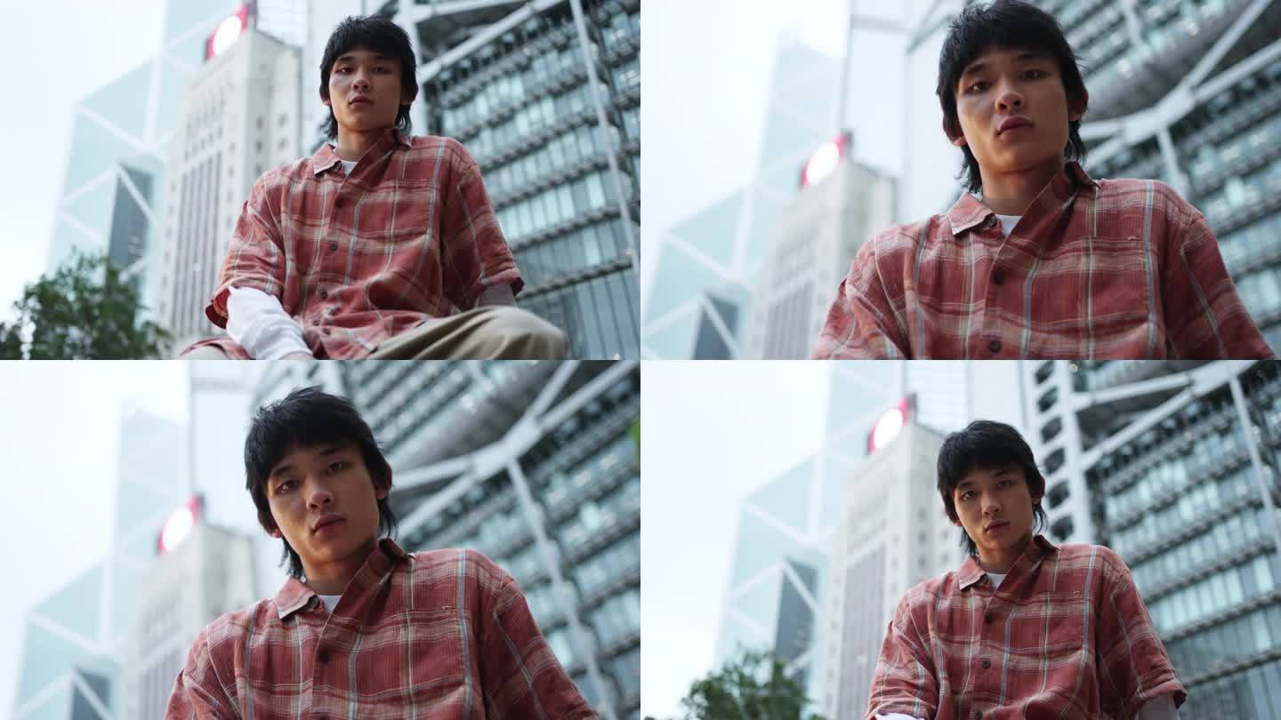 亚洲华人年轻人坐在以香港城市为背景的墙上，目光冷峻