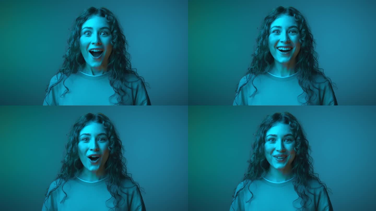 快乐的年轻女子的惊讶肖像，张着嘴看着近距离镜头。一个20多岁的现代女性站在霓虹彩照上的情绪。在蓝色照