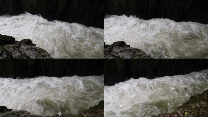 峡谷间湍急的河流。大雨过后，泥土正在往下移。巨大的棕色浑水在大岩石之间翻滚。4k慢动作镜头b滚拍