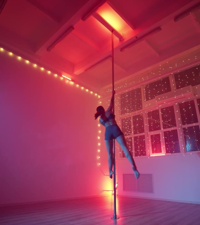 优雅的女子在霓虹灯下跳钢管舞。垂直视频
