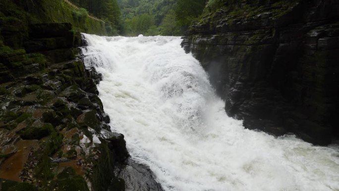 峡谷之间湍急的瀑布河。大雨过后，泥土正在往下移。巨大的棕色浑水在大岩石之间翻滚。4k慢动作镜头b滚拍