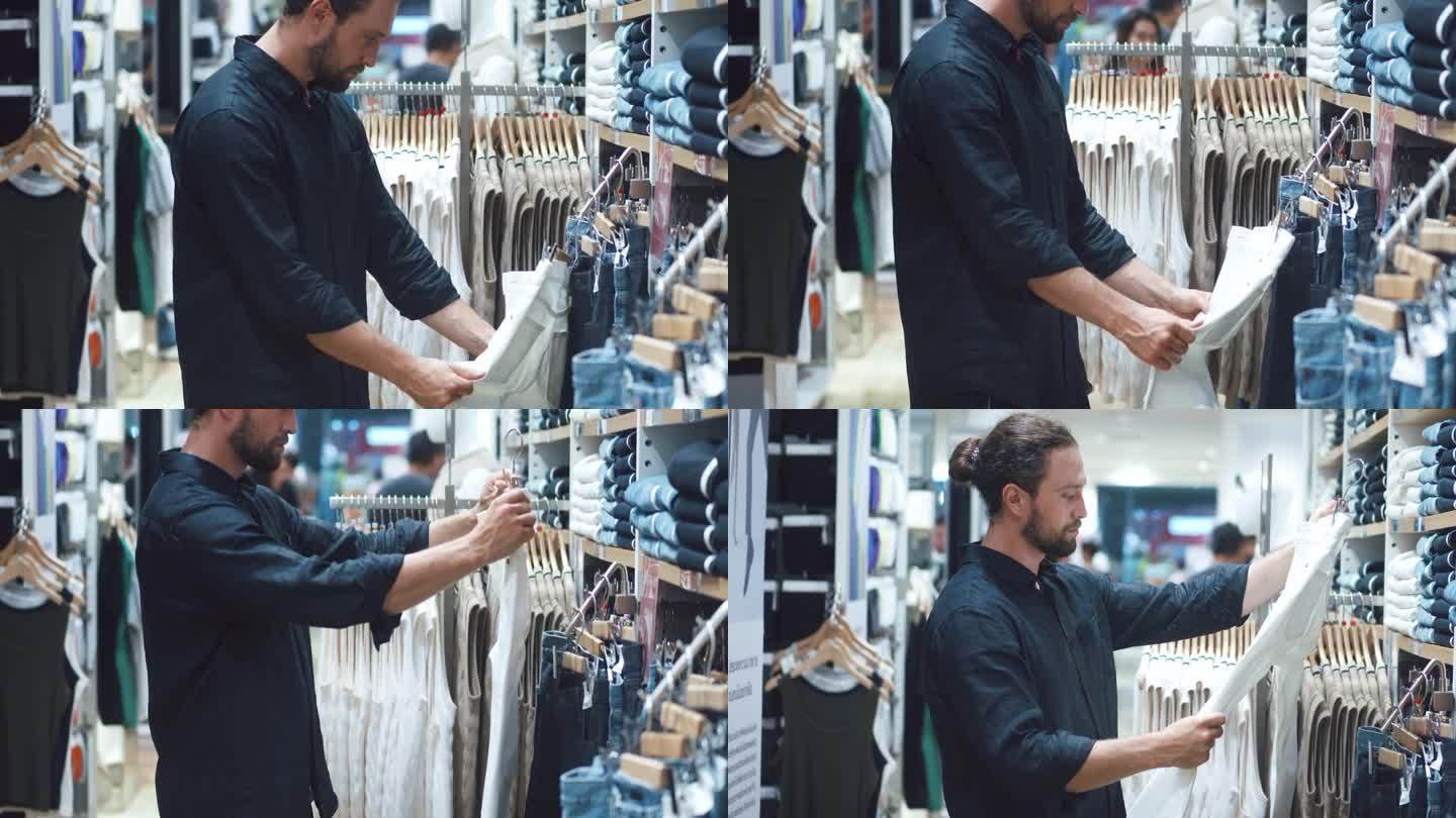 近距离拍摄一位男士在服装店挑选挂在衣架上的牛仔裤。男子在购物中心检查衣服。年轻男顾客在商场试穿新裤子