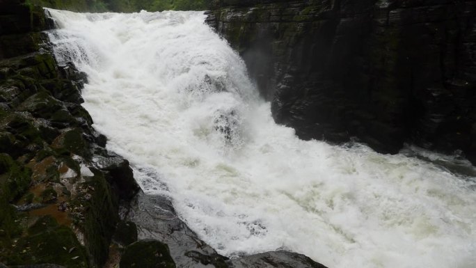 峡谷之间湍急的瀑布河。大雨过后，泥土正在往下移。巨大的棕色浑水在大岩石之间翻滚。4k慢动作镜头b滚拍