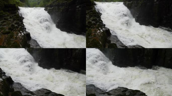 峡谷之间湍急的瀑布河。大雨过后，泥土正在往下移。巨大的棕色浑水在大岩石之间翻滚。4k慢动作镜头b滚拍