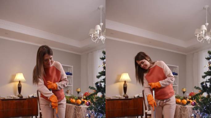 垂直视频。圣诞节前，一位孕妇心情愉快地在客厅里拖木地板。一位妇女站在圣诞树旁微笑。