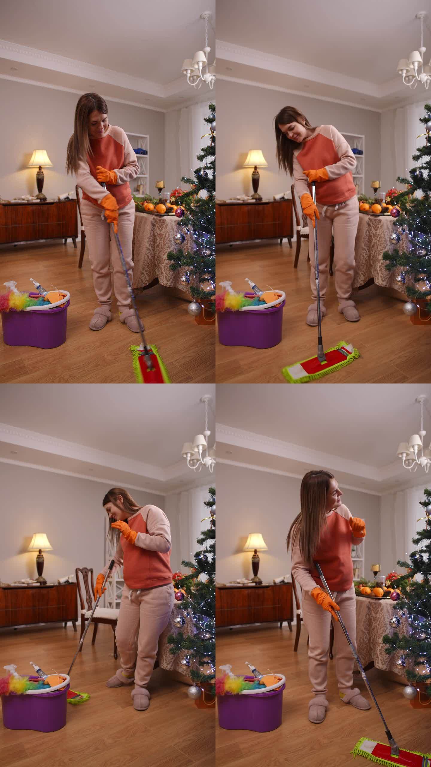 垂直视频。圣诞节前，一位孕妇心情愉快地在客厅里拖木地板。一位妇女站在圣诞树旁微笑。