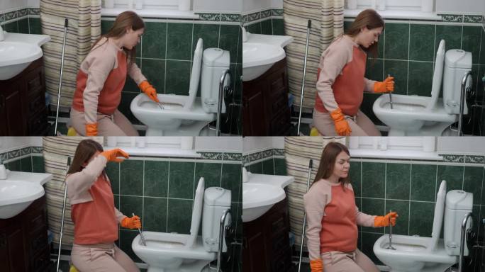一位戴着橡胶手套的孕妇跪在现代住宅的浴室里，用刷子清洁厕所。女人用袖子擦了擦额头上的汗，看着镜头。