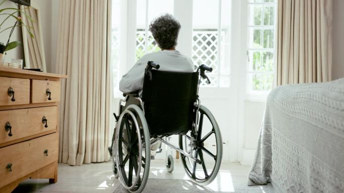 老人，坐在轮椅上思考和人在窗前，孤独在家抑郁。老年人，退休人员和残疾妇女，老年痴呆症或痴呆症在卧室与