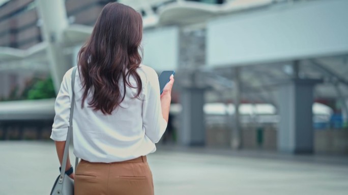 现代都市中女商人用电话走路上班的后视图