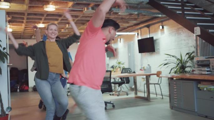 兴奋的同事在现代办公空间庆祝和跳舞