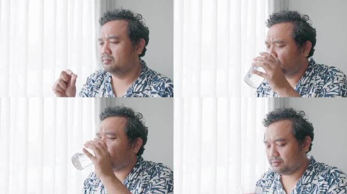 亚洲男人在家里喝一杯淡水吃药。他因头痛而吃了药。补充维生素，为健康滋养身体。医疗保健理念。4 k。