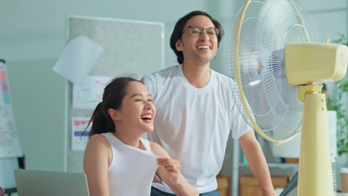 年轻女子和朋友在工作场所享受着风扇带来的空气，商务人士在工作场所的小风扇前受暑。亚洲官员在工作场所开