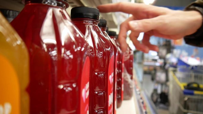 超市里，一名男性顾客的手从一排一排的浆果汁瓶子里拿了一瓶