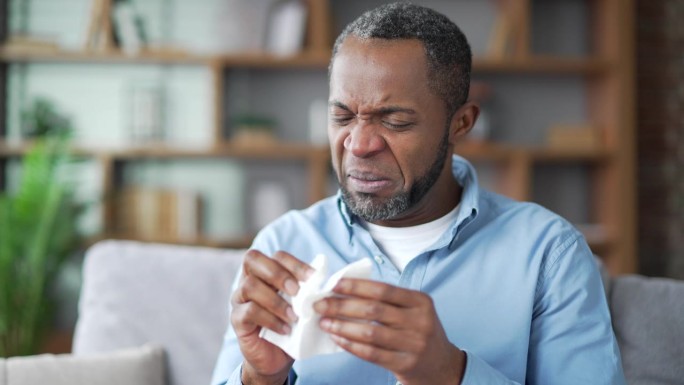 生病的成年非裔美国男性坐在家里客厅的沙发上患有季节性过敏。