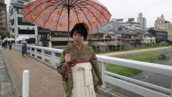 穿着和服/袴的年轻女子穿过加墨河上的桥。