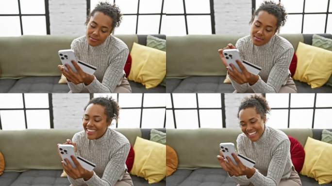 一个微笑的女人在室内用智能手机，拿着信用卡，躺在有彩色靠垫的灰色沙发上。