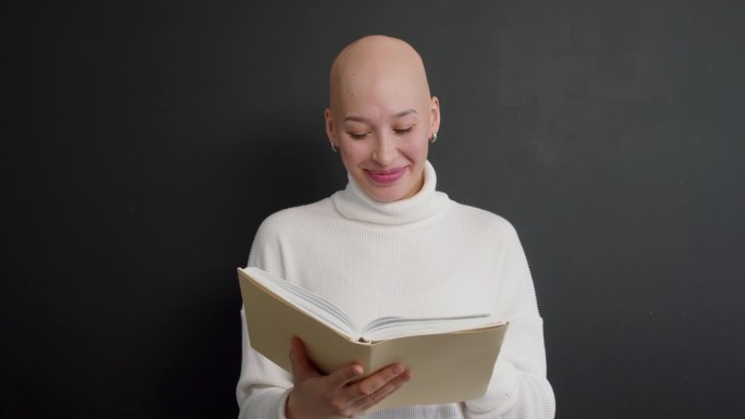 年轻有趣的秃顶女人拿着一本书，笑着，在画室里玩得很开心
