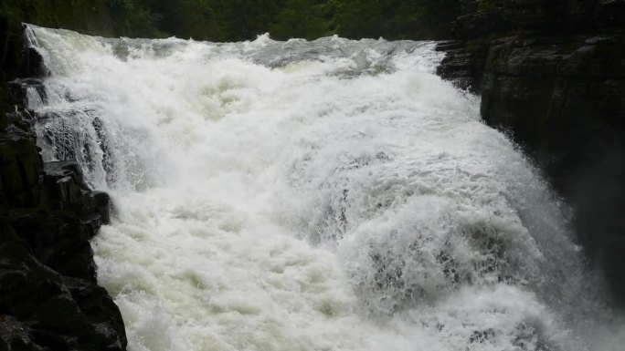 峡谷之间湍急的瀑布河。大雨过后，泥土正在往下移。巨大的棕色浑水在大岩石之间翻滚。4k慢动作镜头b滚拍