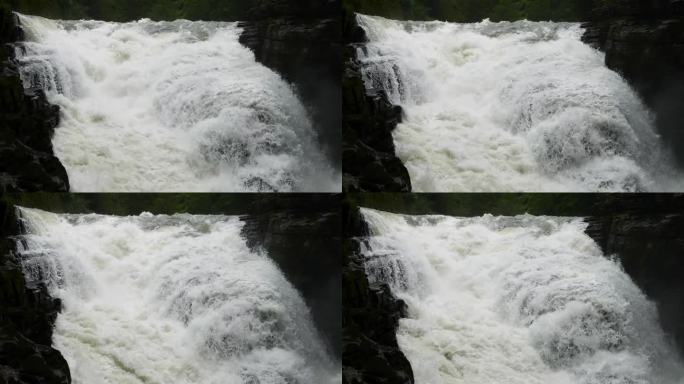 峡谷之间湍急的瀑布河。大雨过后，泥土正在往下移。巨大的棕色浑水在大岩石之间翻滚。4k慢动作镜头b滚拍