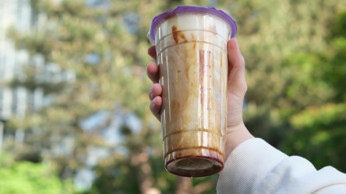 泡沫奶茶塑料杯鲜奶配黑光黑糖浆和波巴热黑珍珠，以摩天楼城市为背景，在一个女孩手中，展现台湾的饮酒文化