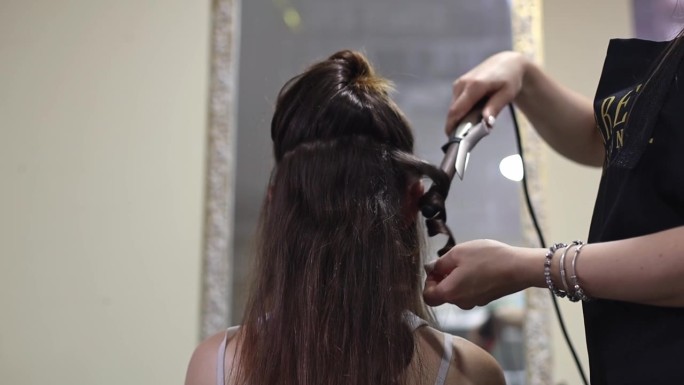 发型师从卷发棒上解开一缕女孩的头发，给她做头发。