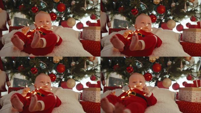 手持拍摄可爱的男婴在圣诞老人的服装玩与背景装饰的圣诞灯