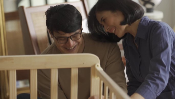 一对亚洲夫妇在育婴室一起组装DIY婴儿床