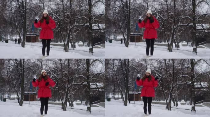 快乐漂亮的女性在下雪的冬季公园行走的全长肖像，视频用智能手机与朋友通话，讲述生活中的故事。与朋友交流