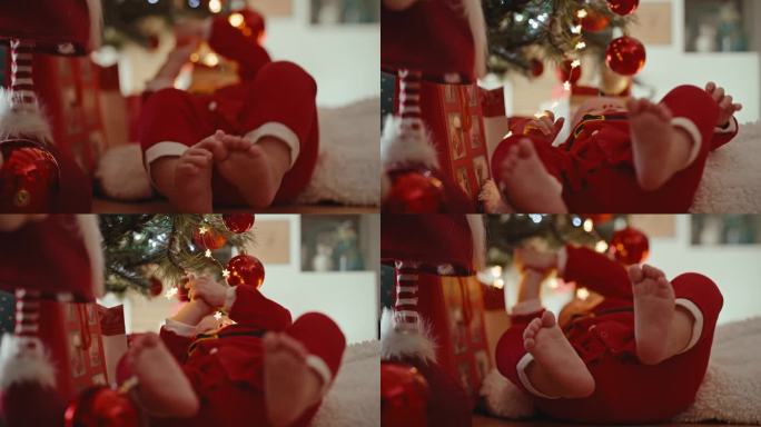 手持架焦点的男婴在圣诞老人服装玩圣诞灯和小玩意，而躺在家里的地板上