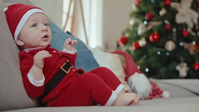 快乐可爱的小男孩穿着圣诞老人的服装坐在家里的沙发上过圣诞节。圣诞快乐，新年快乐，童年快乐，节日快乐，