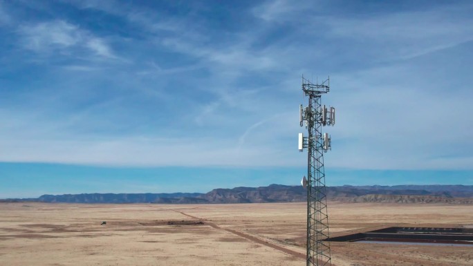 在一个阳光明媚的冬日，犹他州沙漠中一座5G蜂窝塔的无人机照片，天空充满了戏剧性的云层