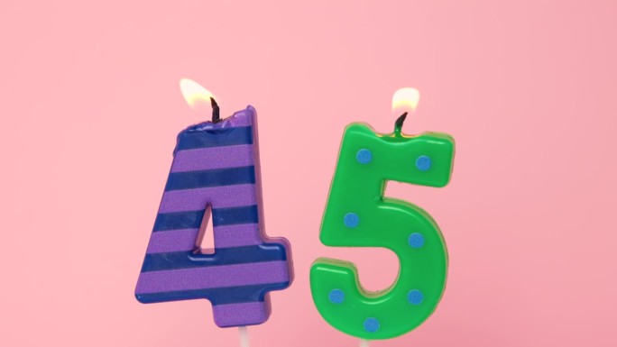 45周年纪念视频横幅燃烧斑点绿色和条纹紫色蜡烛。浅粉色背景上的45号蜡烛。4K分辨率生日快乐横幅。