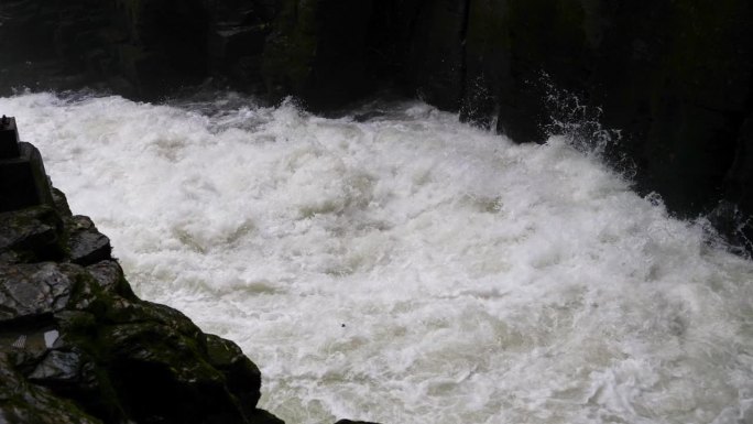 峡谷间湍急的河流。大雨过后，泥土正在往下移。巨大的棕色浑水在大岩石之间翻滚。4k慢动作镜头b滚拍