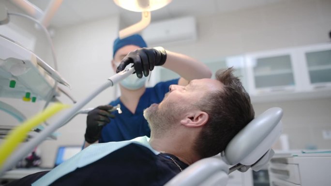 医疗中心的牙医和病人。医生用牙科工具为一个成熟男人的牙齿做专业的口腔卫生。牙齿深层清洁程序