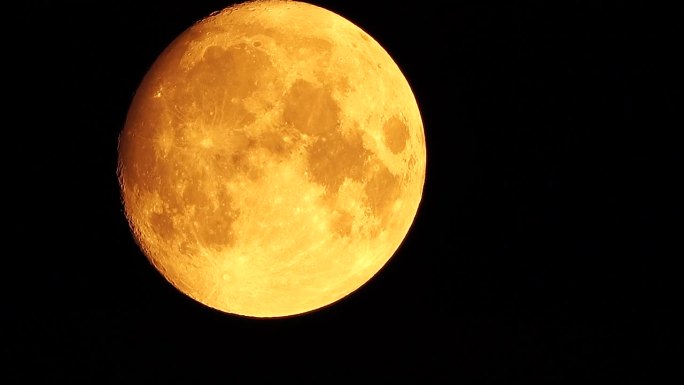 从地球上透过大气层看到的金色满月，映衬着繁星点点的夜空。一轮巨大的满月划过天空，月亮从左下角移动到右
