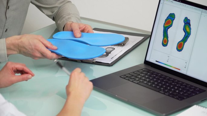 医生在诊所咨询男性患者定制矫形鞋垫，使用笔记本电脑上的测试图片进行个性化定制。足部娱乐医学理念