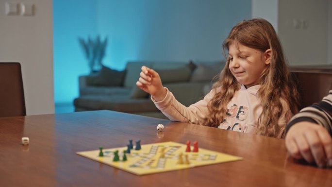 快乐的女孩在桌上掷骰子玩棋盘游戏与家人在家里