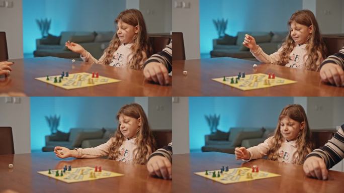 快乐的女孩在桌上掷骰子玩棋盘游戏与家人在家里