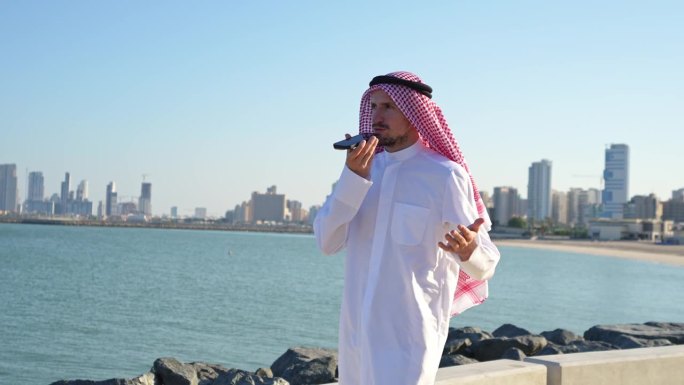 在科威特城的海岸上，一名阿拉伯男子戴着传统的阿拉伯头巾发出语音信息