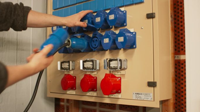 电气面板与蓝色16A和红色32A三相连接器和配电箱。技术人员将三根16A电缆连接到相邻的插座。