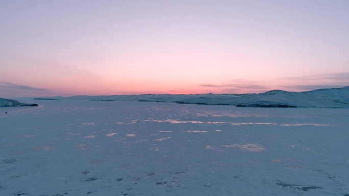 从空中俯瞰冰冻的贝加尔湖，欣赏美丽的粉橙色日出。太阳在冰面上的反射。贝加尔湖冰冻的冬季景观