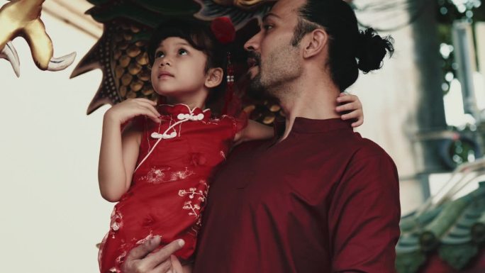 年轻的爸爸抱着她可爱的小女儿看着龙雕塑