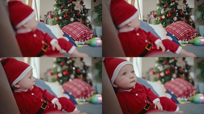 手持架焦点拍摄装饰圣诞树和可爱的婴儿男孩在沙发上的圣诞老人服装在家里