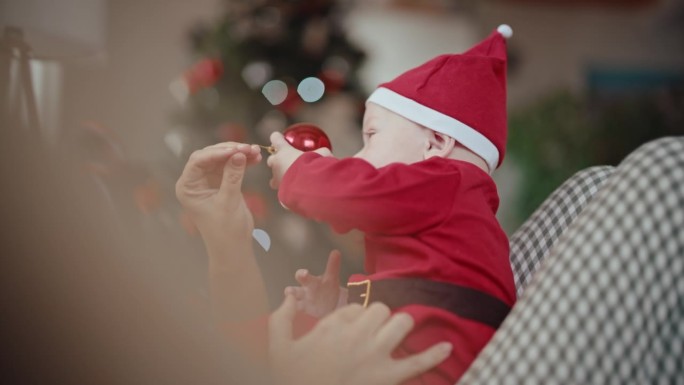 穿着圣诞老人服装的可爱小男孩坐在妈妈身上玩红色小玩意的手持照片