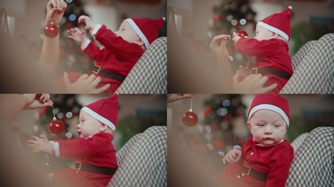穿着圣诞老人服装的可爱小男孩坐在妈妈身上玩红色小玩意的手持照片