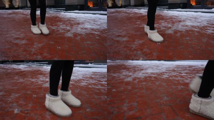 特写镜头中，一个无法辨认的女人穿着冬鞋走在滑溜溜的城市人行道上。女性沿着冰面行走的特写镜头。