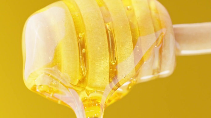 健康的有机蜂蜜。蜂蜜从黄色背景的蜂蜜勺中滴下。