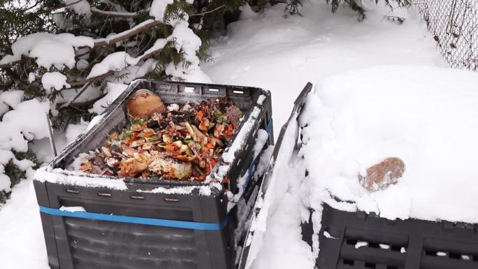 展示开放的堆肥箱与生物废物在室内，室外在冬天，下雪寒冷的天气。