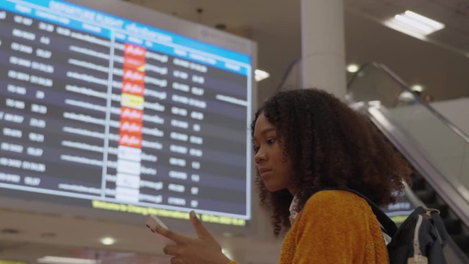图为，机场的黑人女性正在查看数字屏幕上的航班号。