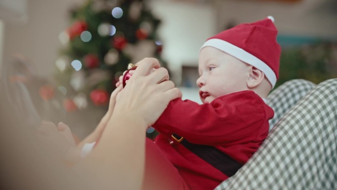 穿着圣诞老人服装的可爱小男孩坐在妈妈身上玩小玩意的手持照片